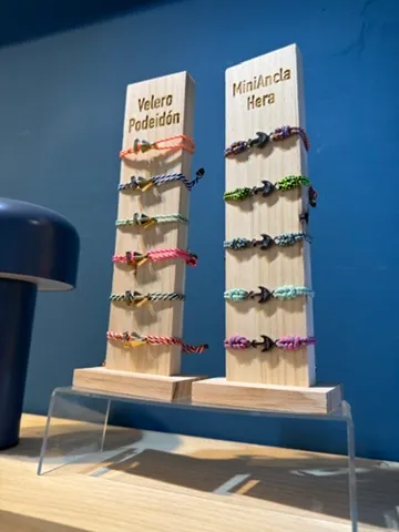 Dos expositores de madera con pulseras de cuerda de colores, uno con el rótulo Velero Poseidón y otro con MiniAncla Hera