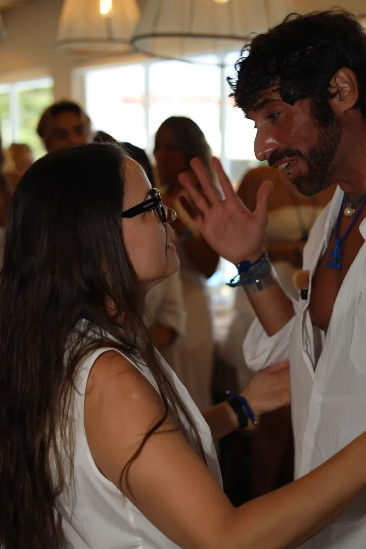 Mujer con gafas y vestido blanco charlando con un hombre de barba y camisa blanca con pulseras de cuerda en la muñeca