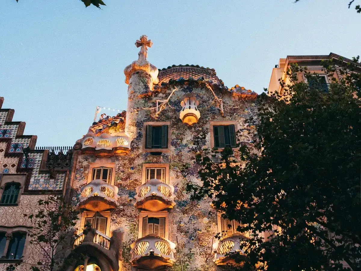 Fachada de la Casa Batlló de Gaudí iluminada al anochecer, con balcones en forma de máscara y mosaico de colores