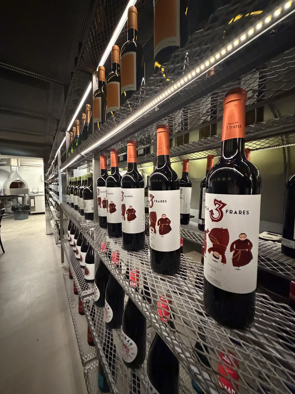 Estantería metálica iluminada llena de botellas de vino en la entrada de Pizzabar