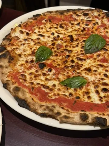 Pizza fina de tomate y queso con hojas de albahaca y el borde tostado en Pizzabar